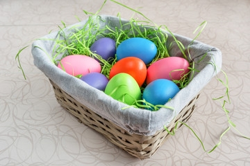 Easter wicker basket with colored eggs on white board.