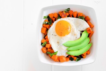 Breakfast nutrient bowl with sweet potato, egg, avocado and spinach above view on white wood