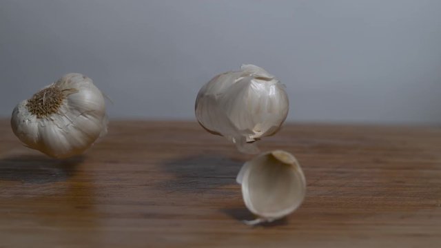 Cloves of garlic falling in slow motion onto a cutting board, moving shot