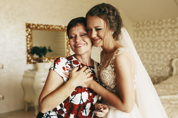 Happy mother holds bride's hand standing with her in the room