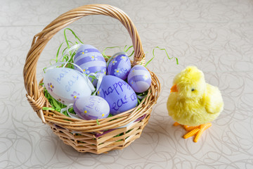 Easter wicker basket with colored eggs and a small chicken on white board.