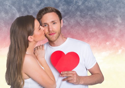 Woman kissing while man holding a red heart