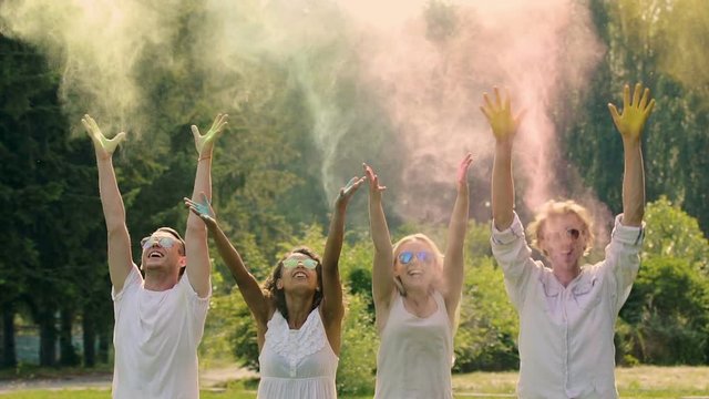 Four young people spraying the colorful powder in extra slow-motion, Holi fest