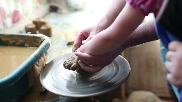 Senior potter teaching happy little girl the art of pottery. Child working with clay, creating modeling ceramic pot on sculpting wheel. Mentoring generations concept. Pottery lessons workshop for kids
