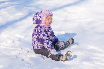 Fototapeta na wymiar Little girl sitting on the snow and laughing
