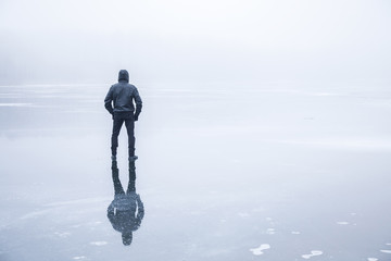 Man in the mist walking on the lake ice in winter afternoon. Peaceful atmosphere. Foggy air.