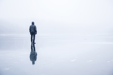Man in the mist walking on the lake ice in winter afternoon. Peaceful atmosphere. Foggy air.