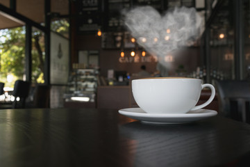 Coffee cup on the table at the coffee shop with heart shaped smoke vintage color tone.
