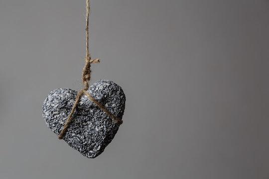 Stone heart in jute bondage hangs against grey background with copy space, Valentine's day concept,