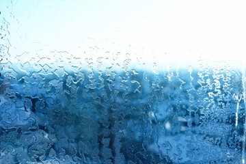 Small pieces of ice melting on the glass windows on the background of the street in the cold tones of blue