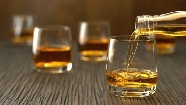 Pouring whiskey into the glass on a wooden table