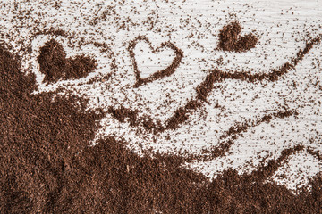 Heart created from ground coffee on the wooden table in the kitchen. Enjoying a coffee break.