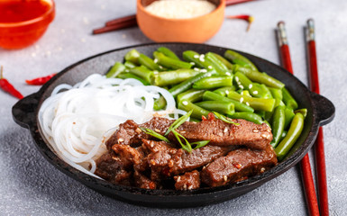 Fried spicy beef with sesame seeds, green beans and rice noodles. Dinner in the Asian style. Selective focus
