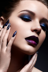 Young woman with creative make-up and violet lips with a gradient and sparkles on the face. Beautiful model with bright nails with rhinestones. The beauty of the face. The photo was taken in a studio.