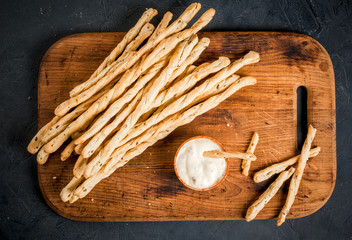 Traditional Italian snack, bread - grizzini. On the kitchen chopping board with sause. On a dark stone table, copy space