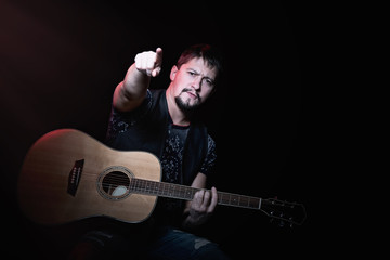 Obraz premium Bearded guitarist with an acoustic guitar in concert indicates the index finger on viewers