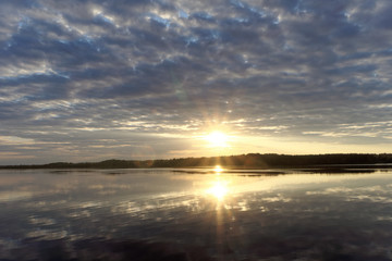 Fototapeta na wymiar View of the golden sunset on the river with clouds and the Sun reflected in it, Volga, Russia