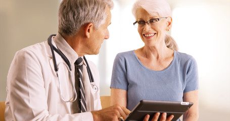 Doctor going over elderly woman's health file in the office with tablet