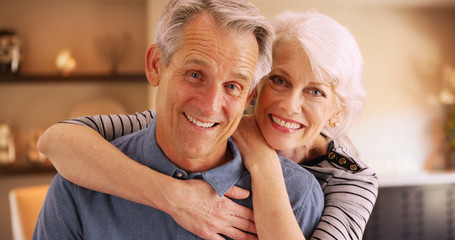 Happy elderly couple sitting at home smiling at camera