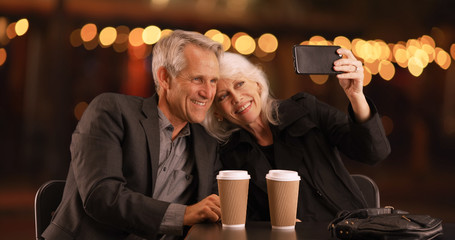 Senior couple out on an evening date taking selfies with smartphone