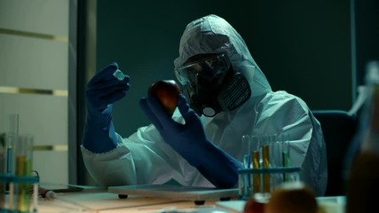 Genetically modified vegetables and fruits. Modern laboratory with engineer in protective clothing testing new additives on artificial apple. He injects colored solution into flesh using syringe or - Powered by Adobe