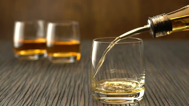 Pouring whiskey into the glass on a wooden table