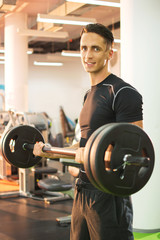 Naklejka na ściany i meble Young handsome man workout with barbell at gym.