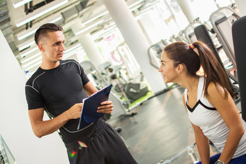 Personal trainer explaining exercise results to his female client in a gym.