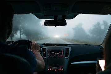 A traveler couple in the car on the way home in fog. Back view