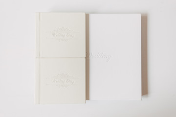 White classic big wedding book in white background. Nearby are two small wedding gift from the bride books for parents
