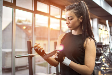 Young fitness lady putting on a sport gloves in gym.