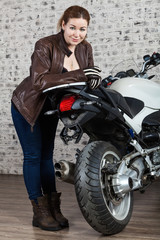 Plakat Female motorcyclist with protective vintage brown leather jacket, boots and gloves standing near a modern motorbike. Full-length portrait