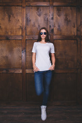 Young woman wearing blank white t-shirt with area for your logo or design, mock-up of template white t-shirt, wooden wall in the background