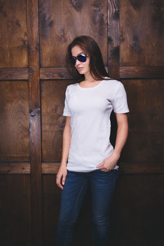 Young woman wearing blank white t-shirt with area for your logo or design, mock-up of template white t-shirt, wooden wall in the background