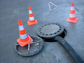 Verkehrsleitkegel, Pylonen oder Lübecker Hütchen sichern einen offenen Kanaldeckel bei der...