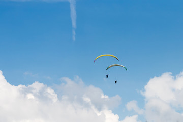 Two people parasailing under blue sky over white clouds
