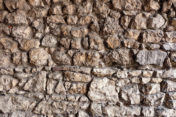 Irregular texture / pattern of a stone wall made of stacked stone blocks / cobblestone. The surface of the stones is rough, resembling the wall of an antique fortress or ancient castle.