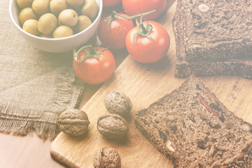 Homemade bread, walnuts, tomatoes and olives in bowl on wooden board