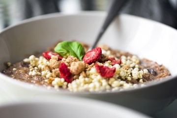Chocolatiers breakfast with oatmeal, puffed rice, cereals and dried strawberries   in a white bowl.  
