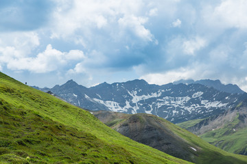 Cloudy sky over green hills in the Italian Alps. A tiny hiker can be seen on the hill.