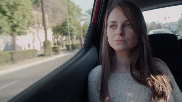 Beautiful woman looking outside through the window in the backseat of a car. She looks worried and sad.