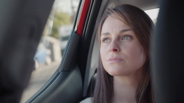 Beautiful woman looking outside through the window in the backseat of a car. She looks worried and sad. Close up.