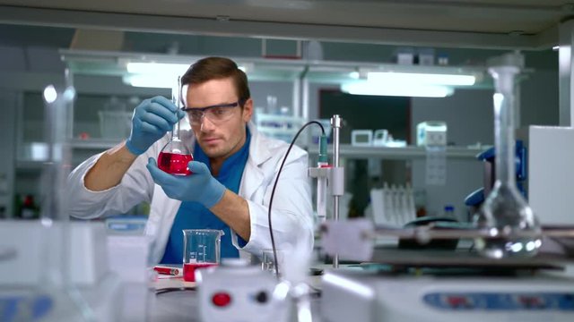 Chemist studying liquid in glass flask at modern lab. Laboratory worker finding a cure. Scientist working at research laboratory. Doctor doing medical research at science lab. Chemistry lab