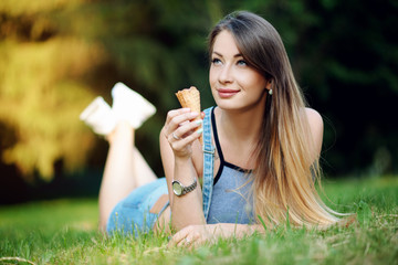 Young beautiful girl in the summer in the park eating ice cream and lying on the lawn