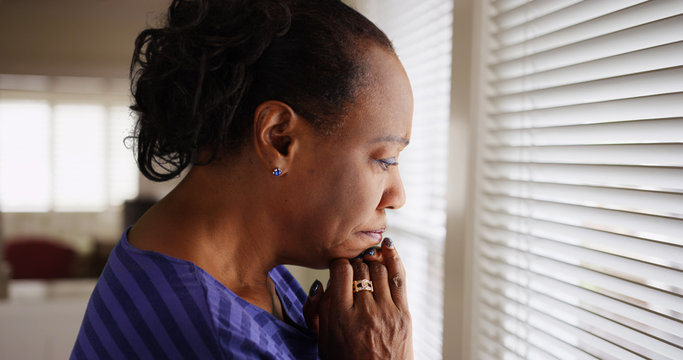 An older black woman mournfully looks out her window