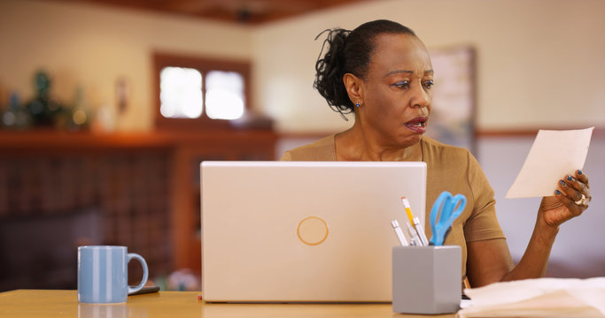 An older black woman sitting in front of computer shocked by bill payments