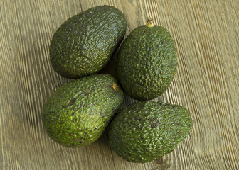 Four Avocados gathered in center of wood