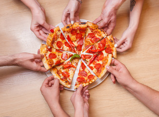 Many hands are taking delicious pieces of pizza