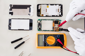 Person Checking Damaged Mobile Phone With Digital Multimeter