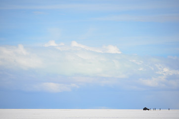 Fototapeta premium Céu azul com núvens no salar de Uyuni com pessoas e carro à distância